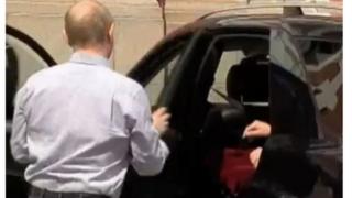 Президент Путин открывает пассажирскую дверь для машины с чем-то вроде красной сумки или платья.