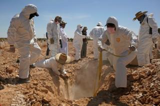 Forensic workers prepare to bury unclaimed bodies in a mass grave.