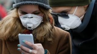 People wearing protective face masks use a smartphone on a street amid coronavirus concerns in Kiev