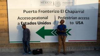 Dos haitianos esperan cerca del acceso peatonal a EE.UU. desde Tijuana.