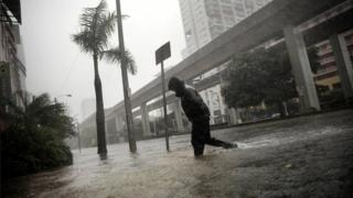 Joven atravesando calles de Miami en medio de la lluvia.