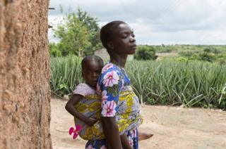 Christy Ansah carries her youngest daughter next to a farm