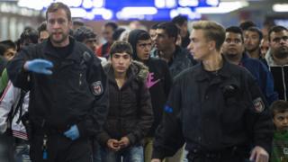 Немецкие полицейские ведут группу беженцев через региональную железнодорожную станцию ??Шенефельд под Берлином.