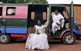 A groom and bride pose in front of a colourful mini van