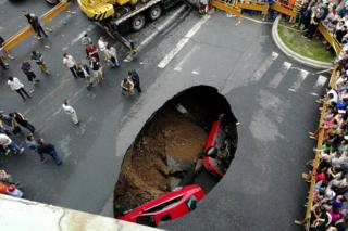 People gather near the scene where two vehicles fell into a sinkhole on a street in Harbin, Heilongjiang province