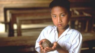 Menino do Laos segura um modelo de bomba de fragmentação