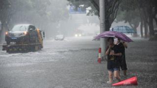People holding umbrellas wade through floodwaters amid heavy rainfall on a street after super typhoon Lekima made landfall in Ningbo
