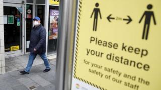 A man walks past a sign in Liverpool reminding people to keep their distance