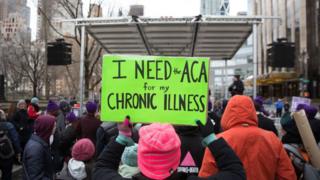 A health care activist lifts signage promoting the Affordable Care Act during a rally at Trump Tower in New York.