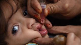Взрослая рука использует маленький шприц, чтобы опустить оральный полиомиелит в рот ребенка в Карачи, Пакистан