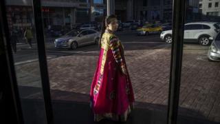 Una norcoreana trata de captar la atención de los viandantes en la ciudad china de Dandong, para que entren a su restaurante.