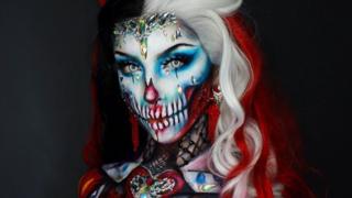 Body painter Ellie pints herself as a bejewelled queen of hearts skull with a red and white wig a crown and a jewelled corset painted to her torso