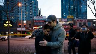 People embrace at the scene of a memorial for victims of a crash at Yonge St. at Finch Ave.