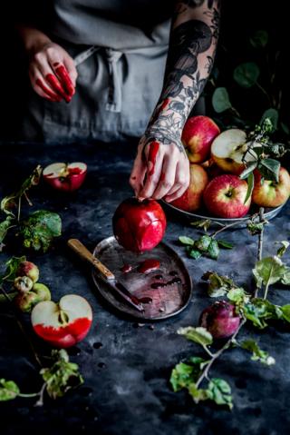 An arm with tattoos on holds an apple that has been dipped in syrup