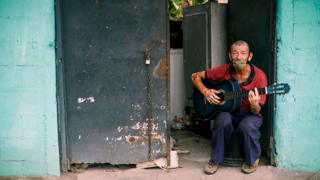 A man wearing a protective mask plays the guitar at his front door in Mejicanos, San Salvador, El Salvador - 7 May 2020