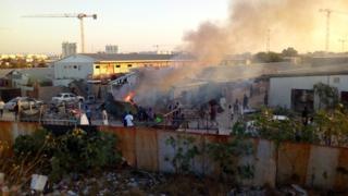 Дым поднимается, когда люди проверяют ущерб после того, как ракета попала в лагерь для перемещенных лиц во время боевых действий между враждующими вооруженными группировками в Триполи 2 сентября 2018 года