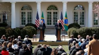 Bolsonaro e Trump no parlatório da Casa Branca, em foto de março, com bandeiras do Brasil e EUA atrás deles