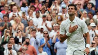 still shows novak djokovic smiling in front of a crowd of people applauding