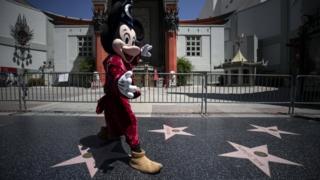 An entertainer wearing a Mickey Mouse costume in front of the closed Chinese TLC Theater on the almost empty Hollywood Boulevard