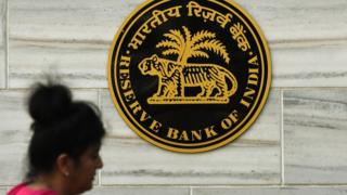 An Indian woman walks past the logo of India's central bank, the Reserve Bank of India (RBI), in Mumbai on November 9, 2016.
