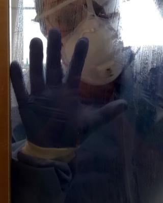 An NHS worker in PPE equipment holds their hand up to the glass in a door