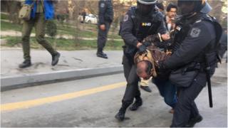 Мужчину, скрутив ему руки за спиной, почти опустив к земле, уводят полицейские