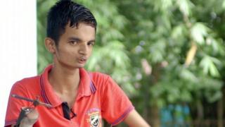 Raj Rehman sitting in a chair. His limb has a device attached to it to allow him the ability to eat