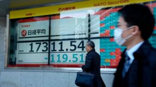 Pedestrians pass a stock markets board in Tokyo (16 March 2020)