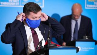 Robin Swann putting on a face mask