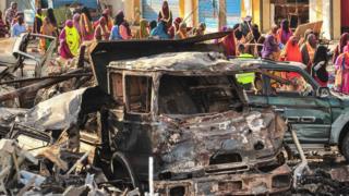 Люди собираются возле сгоревших транспортных средств на следующий день после взрыва бомбы в центре Могадишо