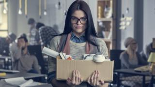 Mujer deja su trabajo con una caja en la mano.