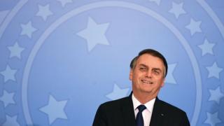 Bolsonaro sorri em frente a painel com brasão