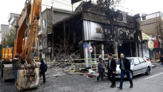 File photo showing people walking past a burned bank in Tehran, Iran (20 November 2019)