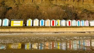 A runner on a beach running past colourful beach huts