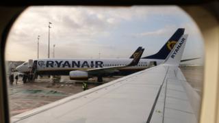 A view of one Ryanair passenger plane on the tarmac, seen through the window of another aircraft looking down the wing