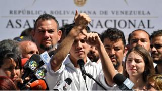 Председатель Национального собрания Венесуэлы Хуан Гуайдо указывает на свое запястье, выступая перед толпой сторонников оппозиции во время открытой встречи в Варгасе