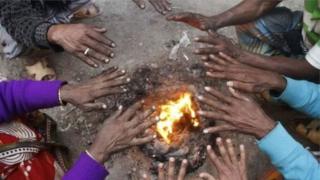 ঠাণ্ডা থেকে নিজেদের বাঁচাতে আগুন পোহাচ্ছেন কয়েকজন