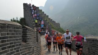 A-group-of-runners-in-brightly-coloured-gear-smile-and-laugh-as-they-run-down-the-steps-of-the-Great-Wall-of-China.