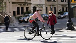 Duas pedestres e uma ciclista com máscaras em rua de Nova York
