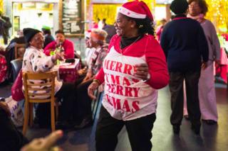 A woman wearing a Christmas hat and top dances in a hall