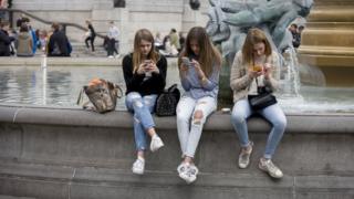 Three teenage girls are lost in the world of smartphone apps and messaging, in Trafalgar Square. While in a very busy environment, the capital's main square in central London, the teenagers obsessively tweet and message their friends at home, completely unaware of their surroundings, absorbed in the functions of their devices and their young lives. Sitting on the walls of the fountains, they are isolated from each other and the noise around them. In the backgrounds are tourists enjoying the arch