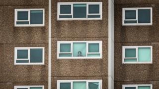 Una mujer en una de las torres de viviendas públicas encerradas en el oeste de Melbourne mira por la ventana