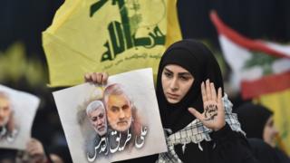 واحدة من أنصار حزب الله ترفع علم الحزب وصورة لقاسم سليماني وأبو مهدي المهندس