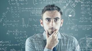 Homem com a mão no queixo, em frente a um quadro com problemas matemáticos