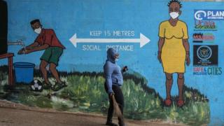 A woman with a face mask walks past graffiti that promotes social distancing, to curb the spread of the COVID-19 coronavirus, in Kibera, Nairobi, on July 15, 2020.