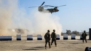 US troops walk as a US Army C-47 Chinook helicopter flies over a village near Mosul