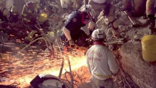 Firefighters use tools to try and blast through remains of building to find victims