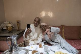 A Moroccan couple talk and waves to relatives on a smartphone as they celebrate Eid al-Fitr at home.
