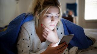 Teenage girl looking at her phone in her bed