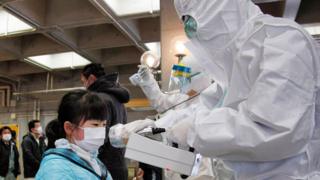 Un funcionario cubierto en un traje de protección nuclear mide los niveles de radiación en una niña